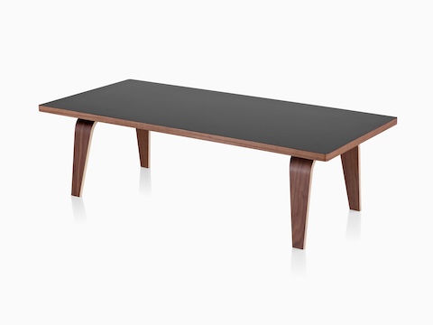 An angled view of an Eames Rectangular Coffee Table with a black top and molded plywood legs in a medium finish. 