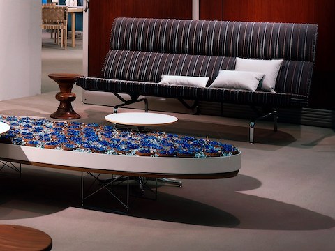 Un sofá Eames Compact con una tela a rayas junto a un taburete Eames Walnut en una sala de trabajo.