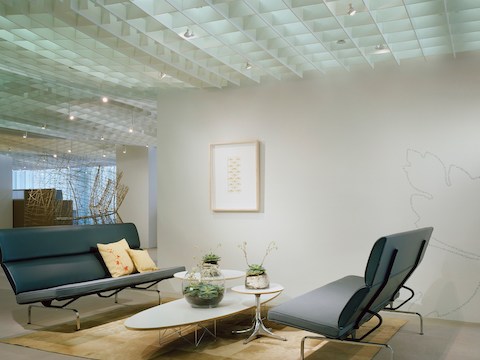 Uma mesa elíptica de base de fio Eames aninhada com duas mesas de pedestal Nelson e posicionada entre dois Compactos de sofá Eames.