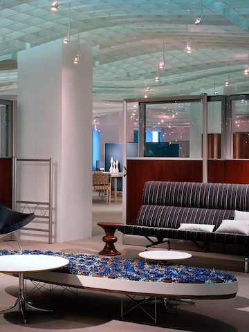 Una mesa elíptica de base de alambre Eames en el vestíbulo de una oficina que también cuenta con un taburete Eames Walnut y un sofá compacto Eames. Una mesa elíptica de base de alambre Eames en el vestíbulo de una oficina que también cuenta con un taburete Eames Walnut y un sofá compacto Eames.