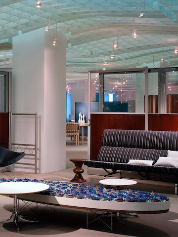 Uma mesa elíptica de base de fio Eames em um lobby de escritório que também possui um Eames Walnut Stool e Eames Sofa Compact.