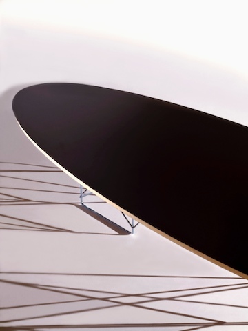 Vista cercana de una mesa elíptica de base de alambre Eames con una parte superior negra, centrándose en el borde biselado.