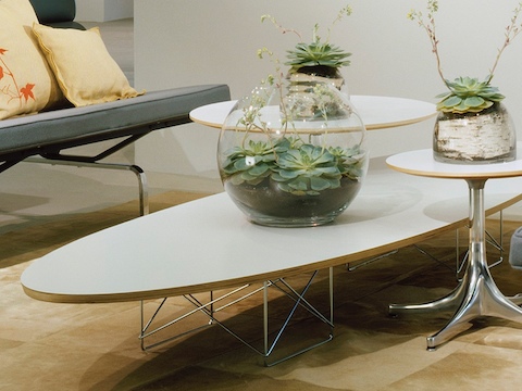 Una mesa elíptica de base de alambre Eames blanca con dos tablas de pedestal Nelson blancas.