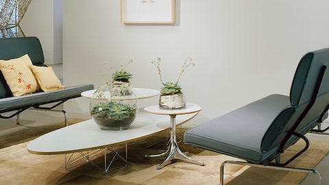 Una mesa elíptica de base de alambre Eames blanca con dos tablas de pedestal Nelson blancas.