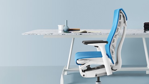 Vue latérale d'une chaise de bureau Embody bleue à une table AGL blanche.