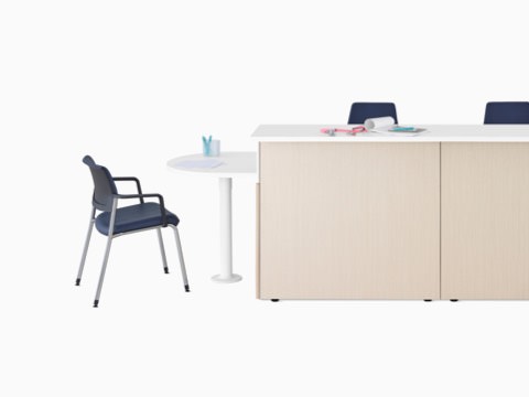 Ethospace Nurses Station in a light wood finish with transaction surface and ADA peninsula surface in white, a Verus Side Chair in blue, and Sayl Chairs in blue.
