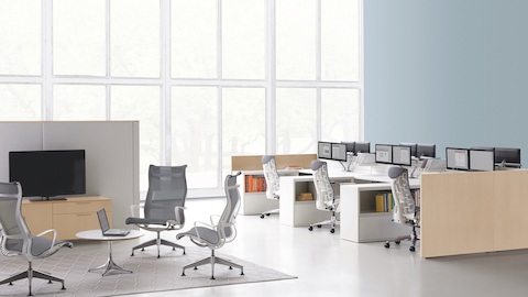 Un salón con Sillones Setu cerca de una serie de espacios de trabajo Ethospace con sillas de escritorio ergonómicas Embody grises.