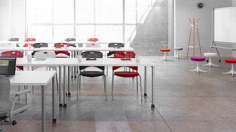 Duas fileiras de mesas Everywhere retangulares em configuração de treinamento e cadeiras empilháveis Caper multicolorias.