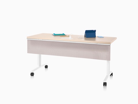 Viewed at an angle, an Everywhere Table with a clear on ash woodgrain top, fabric modesty panel attached to the surface and a white base with casters.