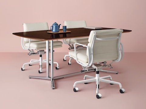 Tres sillas Eames Soft Pad de cuero blanco alrededor de una mesa de reuniones rectangular Everywhere en acabado de madera oscura.