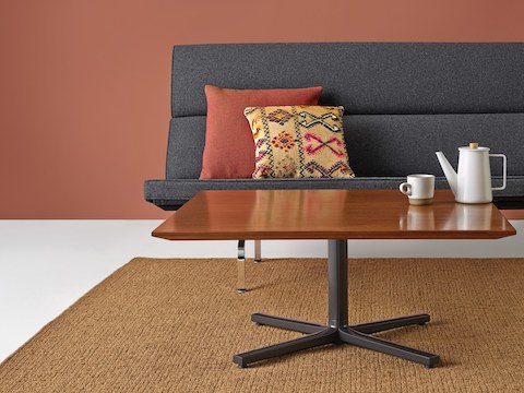 Mesa para visitantes Everywhere com tampo em madeira de nogueira e base em coluna preta simples colocada na frente de um sofá compacto Eames.