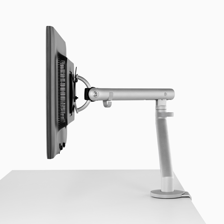 Side profile of a silver, single Flo Monitor Arm holding a screen and attached to a white work surface.