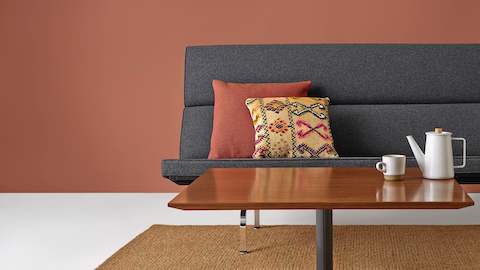 A rectangular Everywhere coffee table in a medium wood finish positioned before a gray Eames Sofa Compact.