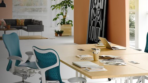 Un espacio de colaboración anclado por cuatro mesas cuadradas Everywhere con un acabado de madera clara, agrupadas para formar una gran mesa de reuniones.