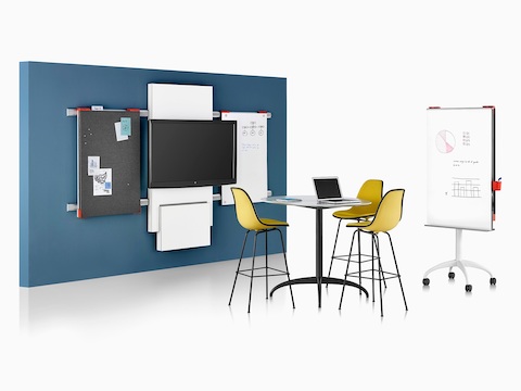 A collaboration space featuring a table, media tile, and display boards from Exclave,  as well as three yellow stools.