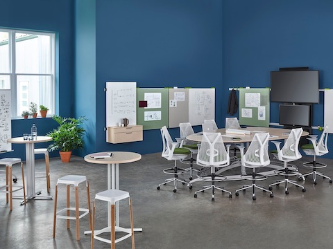 Sayl office chairs surround a teardrop Exclave table in a collaboration space with a wall-hung media tile and display boards.