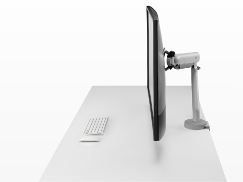 Silver single Flo X monitor arm with a 43'' screen, viewed from the side.