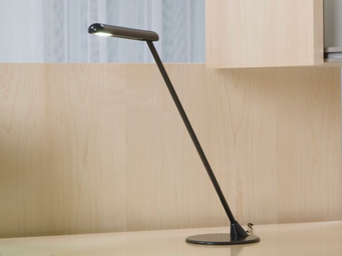 Um Flute Personal Light autônomo preto fornece iluminação direcionada em uma área de trabalho.