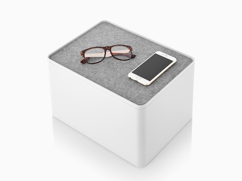 Uno scomparto alto Formwork bianco con una fodera antiscivolo usata come coperchio, che contiene occhiali e uno smartphone.