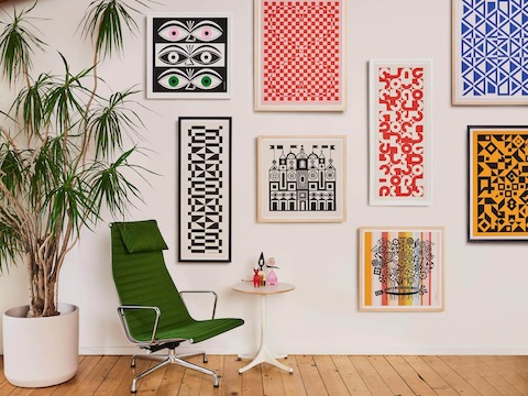 Agrupación de pósters Girard Environmental Enrichment incluidos Ojos, Bouquet y Secciones circulares junto a un sillón lounge Eames Aluminum Group en verde.