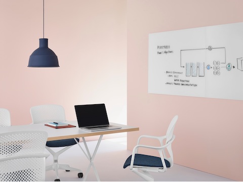 White Keyn Chairs with dark blue upholstery in a meeting space with a Glass White Board with brainstorming sketches on it at the end of a table.