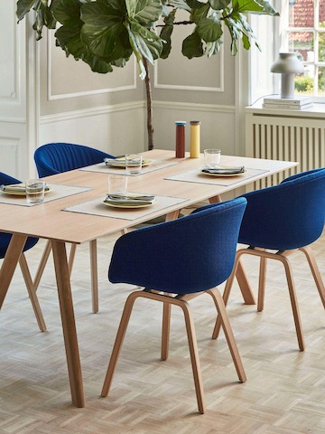 Uma mesa de jantar Copenhague em carvalho com rodeada por cadeiras About A Chair azul marinho.