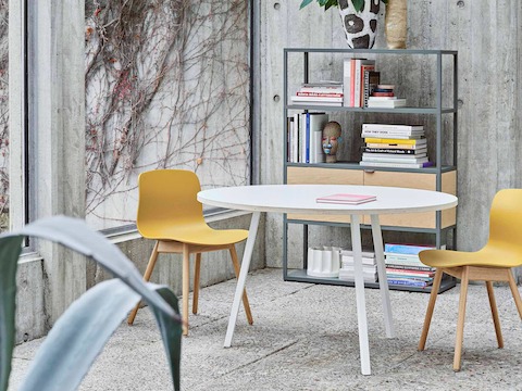 Two yellow About A Chairs with wooden bases are placed in a room with a white, round Loop Stand table.