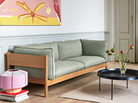 A light green Arbour Sofa with a wood frame, next to a green Dorso Lounge Chair and a black Tulou Coffee Table.