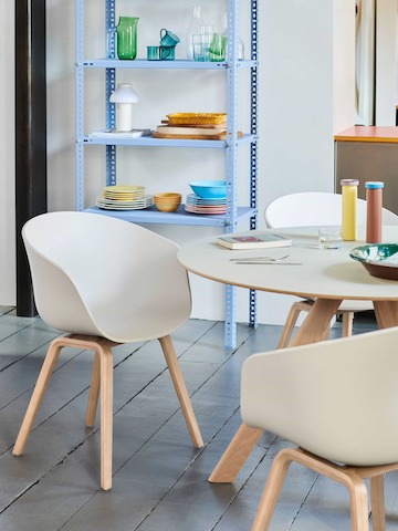 Duas cadeiras About A Chair em branco, ao lado de uma mesa Copenhague – redonda.