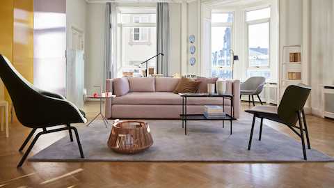 Una sala centrada en torno a un sofá seccional Mags en rosa de HAY con una silla lounge Dapper, visto en ángulo desde atrás, al frente.