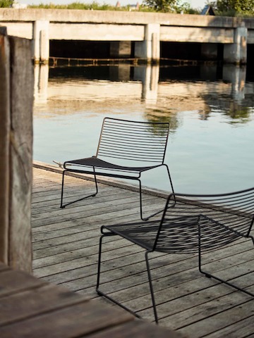 Two black Hee Lounge Chairs next to a river.