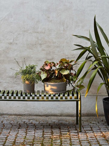 A Palissade Bench outside with flower pots sitting on top.