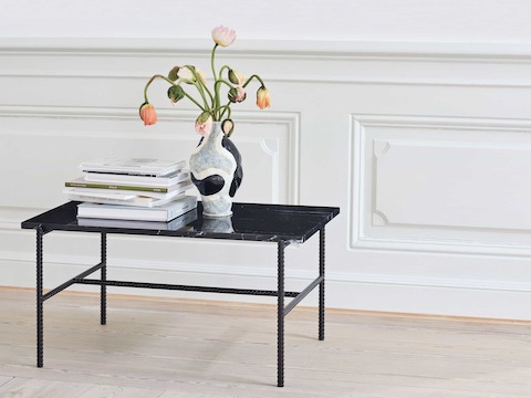 A Rebar side table with black marble top and black frame that has books and a vase sitting on top.