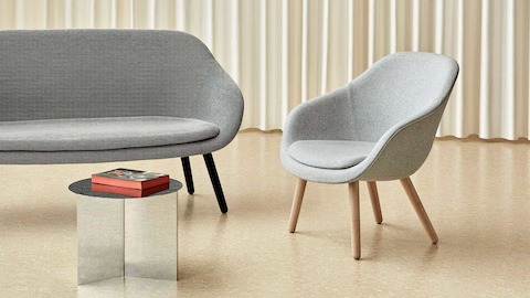 Um sofá About A Lounge cinza com pernas pretas ao lado de uma cadeira About A Lounge 82 cinza com uma mesa redonda Slit no espelho.