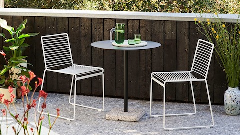 Two white Hee Chairs with a Terrazzo Table in a courtyard.