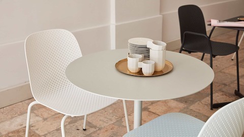 Close-up of white 13Eighty Chairs and a white, round Terrazzo Table. A black 13Eighty Chair with arms is in the background