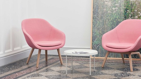 Two pink About A Lounge Chairs with wooden bases, and a Tulou Coffee Table in white.