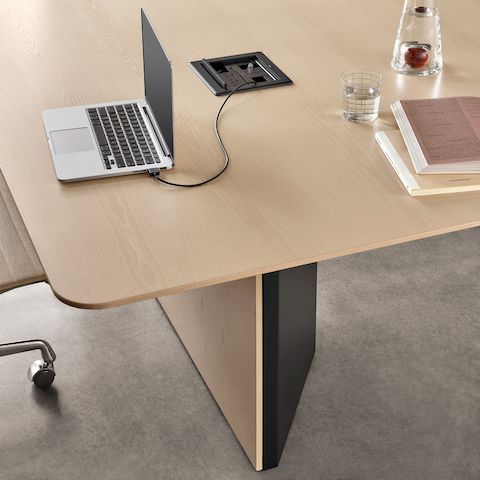 Close-up of a cabinet-base Headway Conference Table, with a laptop on its surface and a tabletop Crestron cord retractor unit for power.