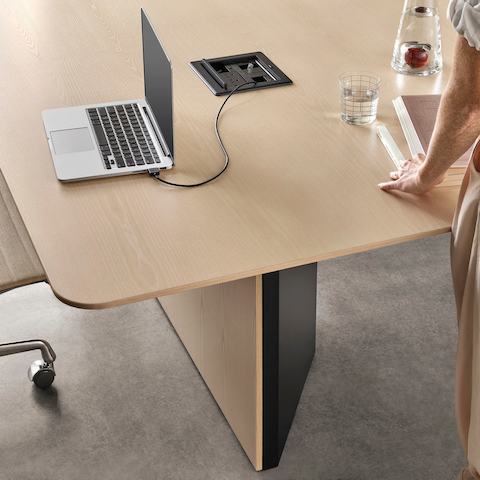 Vista de perto da mesa de conferências Headway com base com gabinete e laptop em sua superfície, conectada a uma unidade retratora do cabo Creston.