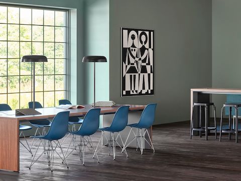 An office setting featuring two Headway communal tables, one seated height and surrounded by Eames Plastic side chairs and the other standing height with black stools. 