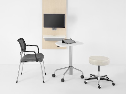 An Intent Solution technology support wall unit in an ash wood finish, an Intent Solution mobile height-adjustable table with a white top and silver base, and a Verus side chair and a physician's stool near the table.