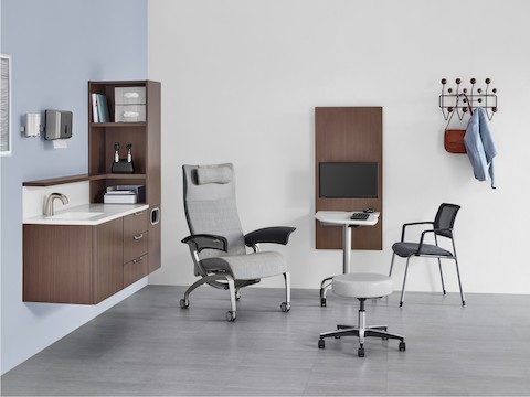 An exam room with Mora System casework in a dark brown finish and an Intent Solution table between a patient chair and side chair.