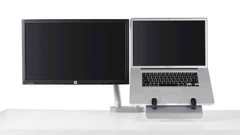 Un brazo con dos monitores eleva tanto la pantalla de la computadora como la computadora portátil, utilizando un soporte para computadora portátil, fuera de la superficie de trabajo.