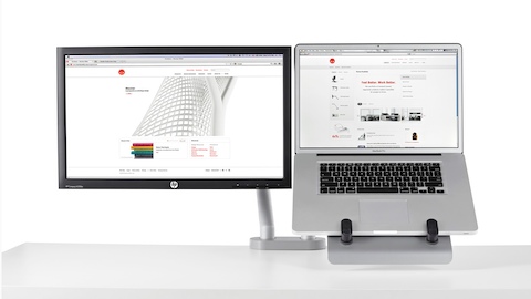 Ein Doppelmonitorarm unterstützt sowohl einen Computerbildschirm als auch eine Laptop-Halterung, in der sich ein Notebook befindet.