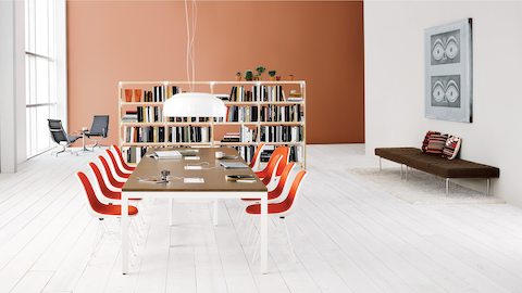 A workshop setting with a Layout Studio project table surrounded by upholstered Eames Molded Plastic Side Chairs and a bookcase in the background.