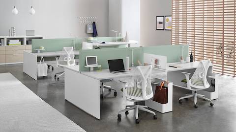 Cadeiras Sayl brancas com almofadas verdes em estações de trabalho individuais Layout Studio em diversas alturas com telas divisórias verdes e mesas brancas.