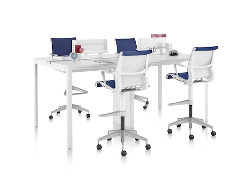 A standing-height Layout Studio bench with white laminate top and legs surrounded by four Setu Stools and two Ubi Attached Shelves in the center.