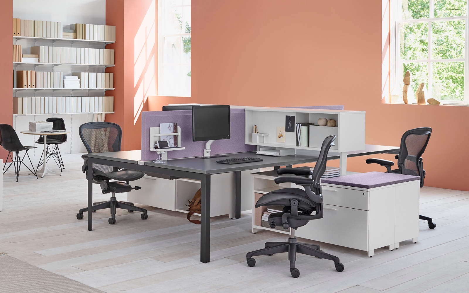 A workspace setting with two Layout Studio benches with purple fabric center privacy screens, Aeron Chairs, and Tu Storage cubbies and credenzas.