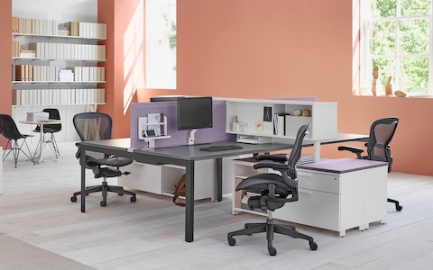 A workspace setting with two Layout Studio benches with purple fabric center privacy screens, Aeron Chairs, and Tu Storage cubbies and credenzas.