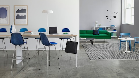 A standing height Layout Studio bench with Eames Molded Fiberglass Stools in the foreground and a lounge space with a Bolster Sofa in the background.